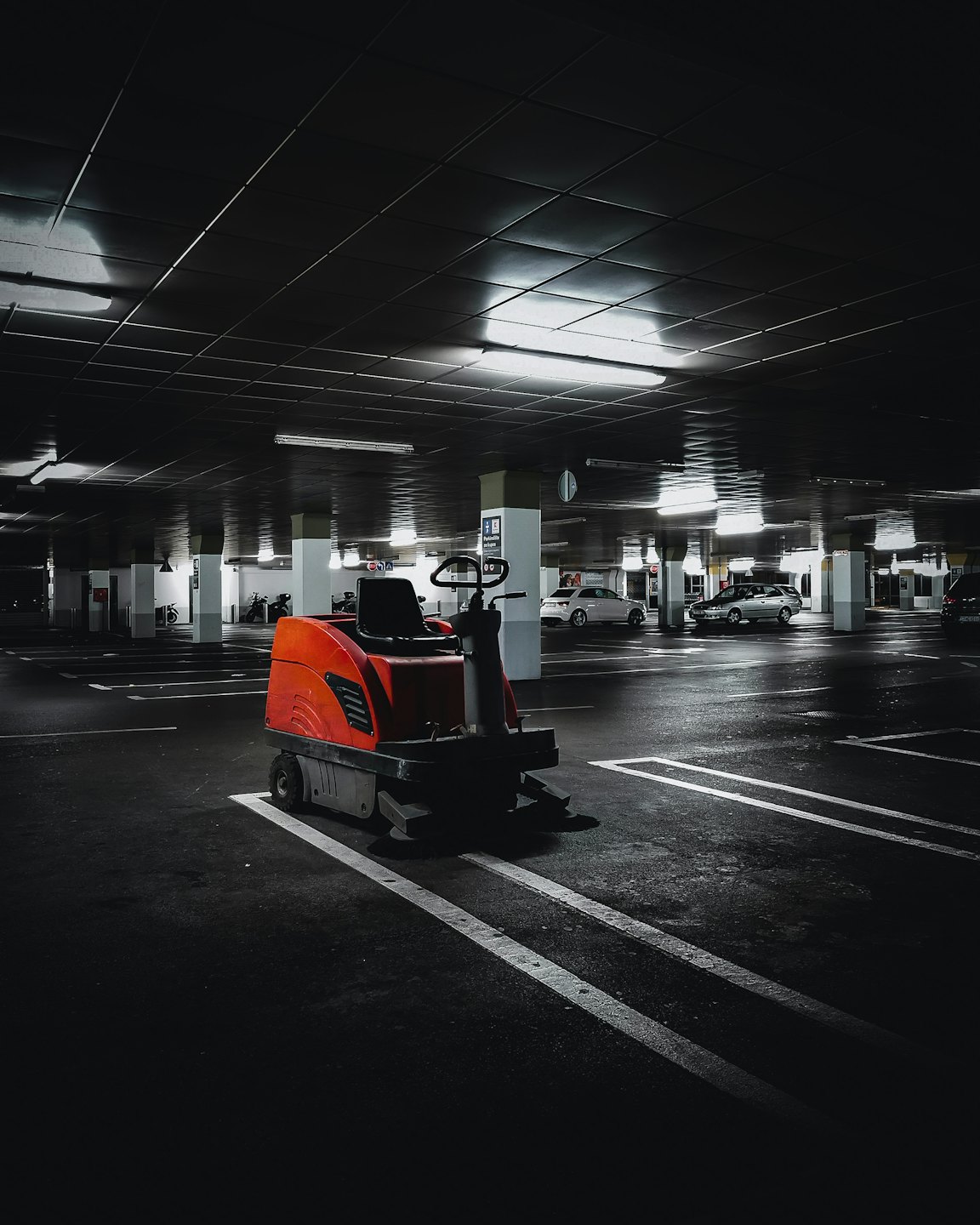 Pomarańczowa przemysłowa maszyna czyszcząca zaparkowana na parkingu podziemnym.